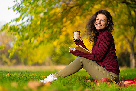 一个可爱的女孩读了一本书 喝着咖啡 在绿草坪上季节闲暇文学女性格子毯子公园学生幸福假期图片