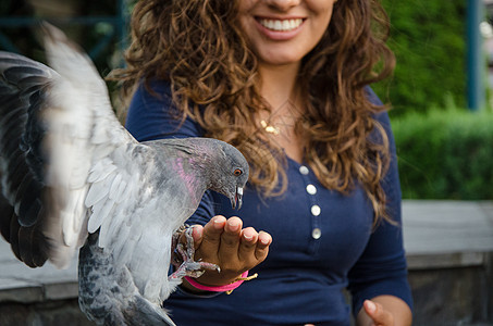 一个微笑的女人从她手里喂鸽子地面动物手臂厨房公园议程自由生活翅膀裂缝图片
