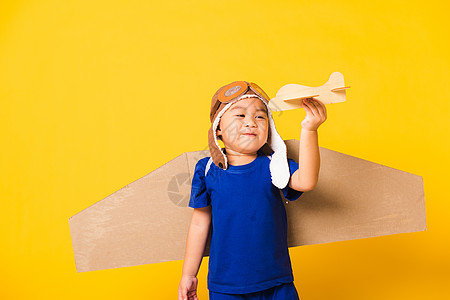 小男孩笑笑 戴着飞行员帽子玩耍 带着玩具卡的护目镜纸板想像力乐趣黄色幸福飞行假期喷射男生孩子图片