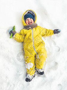 穿着明亮黄色衬衣微笑的小毛孩躺在雪上图片