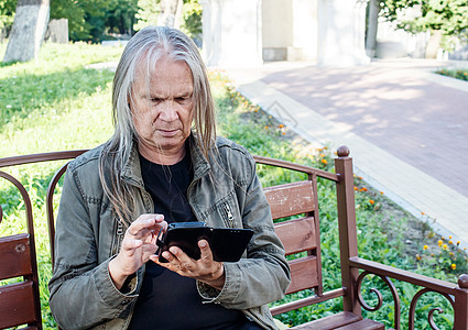 老年男子坐在Ben上时使用智能手机打开应用程序图片