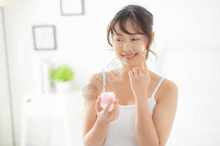 美丽的年轻亚洲女性很高兴在皮肤上涂抹带有保湿霜的面霜或乳液 美丽的亚洲女孩在面部涂抹护肤品和化妆品 健康和健康的概念女士奶油皮肤图片