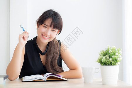 美丽的亚洲年轻女性微笑着坐着学习 在家里的客厅里学习写笔记本和日记 女孩的家庭作业 在桌子上工作的女商务人士 教育理念笔记快乐考图片