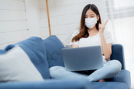 戴面罩的年轻亚洲女商务人士思考想法 在家里用笔记本电脑在线工作 在客厅上网 戴医用口罩的女孩和 covid19 隔离区 待在家里图片