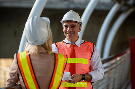 站在建筑工地时戴着白色头盔的女工业工程师与商务人士谈论工作计划 工程师和建筑师在建筑工地概念安全女士安全帽工人金工仓库制造厂技术图片