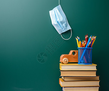 绿色粉笔板背景的可一次性医疗面罩 堆叠书籍和学校文具面具大学铅笔桌子蓝色黑板学习预防笔记本木板图片