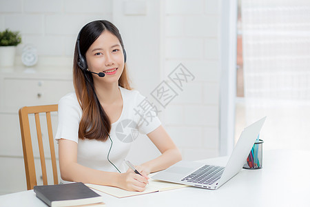 年轻的亚洲女性戴着耳机在线学习 在办公桌上进行电子学习 戴着耳机的女孩在家里用笔记本电脑学习互联网 新常态 远程教育和培训成人教图片