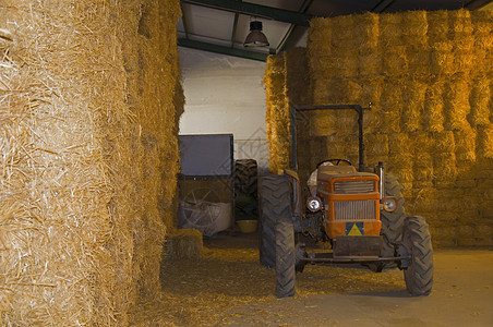 仓库中的小型红色拖拉机和干草堆图片