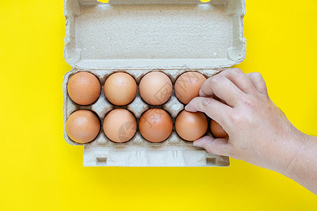 男人的手在纸盒里捡到一个棕色蛋 在黄色背景上宏观生食生长蛋壳女性母鸡动物饮食健康饮食食物图片