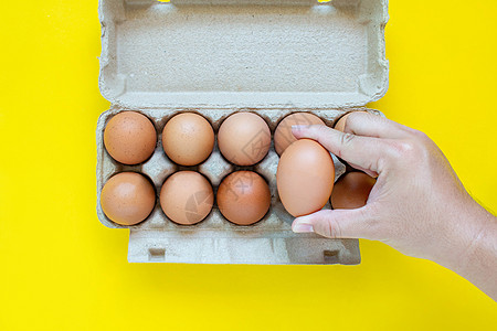 男人的手在纸盒里捡到一个棕色蛋 在黄色背景上女性动物母鸡蛋壳宏观烹饪手指健康饮食食物农场图片