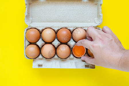 一只男人的手抓住了一个锤子褐蛋 然后把鸡蛋放在纸盒里 在黄色背景上厨房健康饮食食物蛋壳烹饪杂货摄影乡村家禽午餐图片