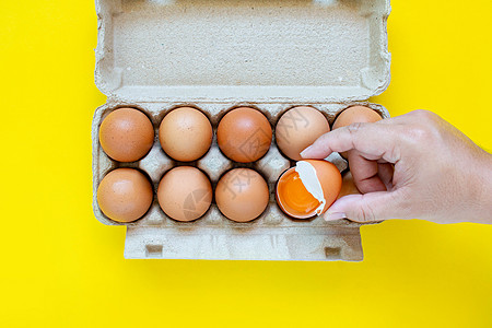 一只男人的手抓住了一个锤子褐蛋 然后把鸡蛋放在纸盒里 在黄色背景上家禽裂缝烹饪动物蛋壳健康饮食早餐杂货饮食午餐图片