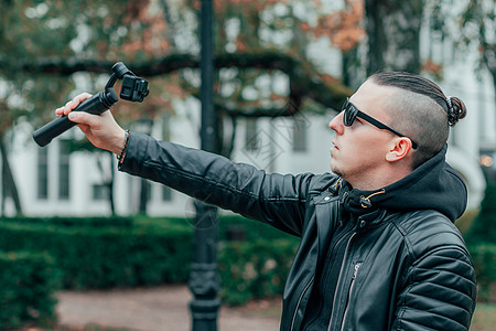 在公园使用行动相机制造自以为是的嬉皮士录像男性博客旅游成人绿色摄影旅行多云博主图片