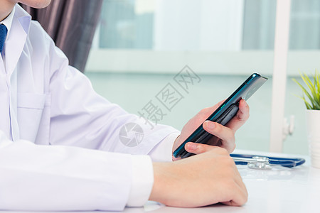 医生用智能手机工作时微笑的女医生裁剪阅读诊所桌子医院电脑医师办公室短信女性图片