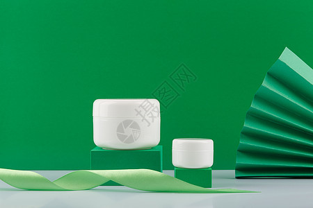 在装饰绿色背景的讲台上的两个奶油罐 天然成分有机化妆品的概念图片