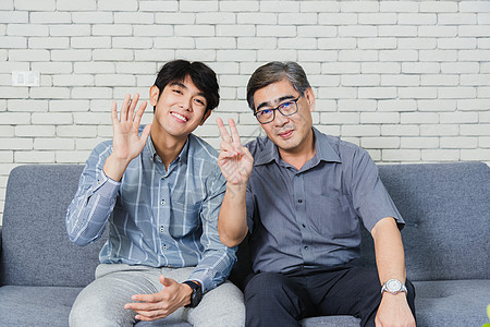 父亲和他儿子坐在沙发上聊天的视频电话互联网父母电影技术长椅成人男人房子男性快乐图片