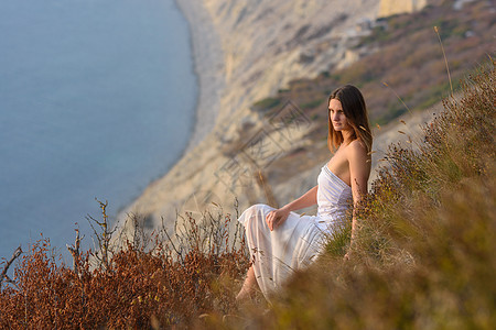 一个穿白裙子的漂亮女孩 在日落时 享受着从山到海的美丽景色图片