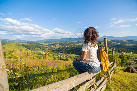 快乐的华丽女孩享受山上风景 坐在山上的花田中 充满了令人惊叹的自然景观自由冒险游客成就情感裙子女性运动栅栏天空图片