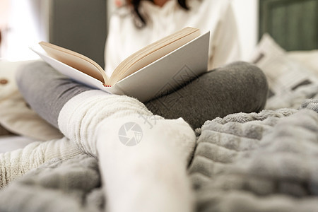 从低角度看 面目全非的女人穿着舒适的衣服坐在沙发上 放松地阅读一本前景模糊的白色羊毛袜的纸质书 有选择地关注封面背景图片