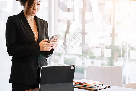 在办公室使用智能手机进行社交或聊天的智能平板电脑上工作的商业女商务人士图片