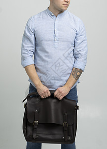 棕色男士单肩皮包 用于存放文件和笔记本电脑 由身穿蓝色衬衫和白色背景牛仔裤的男士携带 挎包 男士真皮手工公文包口袋奢华人士配件书图片
