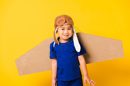 小男孩笑笑时 带着玩具纸板飞机机翼 戴着飞行员帽子玩耍和护目镜冒险领导者飞行自由黄色乐趣幸福喷射想像力创新图片