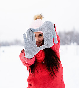 穿着红毛衣的年轻美女 在雪天用手在户外做壁架标志微笑公园衣服快乐帽子冒充喜悦女士假期季节图片