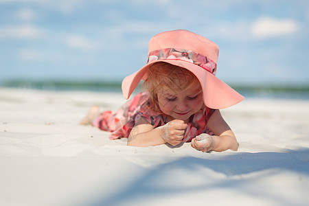 一个穿着漂亮的 sarafna 的小女孩在沙滩上的沙子里玩耍海洋晴天喜悦海滩假期童年支撑乐趣帽子幸福图片