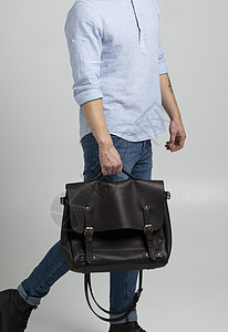 棕色男士单肩皮包 用于存放文件和笔记本电脑 由身穿蓝色衬衫和白色背景牛仔裤的男士携带 挎包 男士真皮手工公文包手提箱办公室皮革背图片
