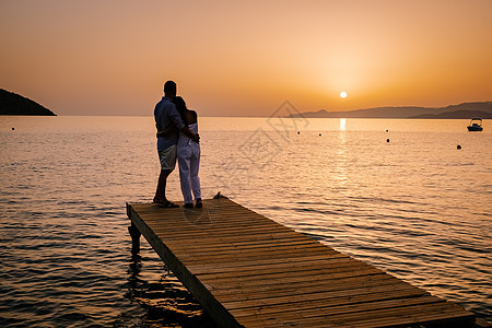 一对夫妇坐在木制码头上 看着海边多彩的日落 男人和女人在希腊克里特看日落海洋夫妻男性女性木头蜜月幸福阳光热带朋友们图片