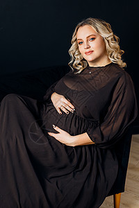 在室内工作室黑墙背景下 穿着高雅黑色衣服的女孕妇腹部成人女性沙发新生活魅力妈妈母性数字怀孕图片