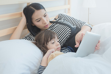 快乐的亲友 像亚洲年轻的母亲 在智能平板电脑上看卡通 她的女儿在节假日图片