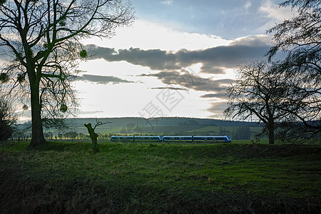 一辆移动的现代区域列车 在一片绿地和阴云的天空中图片
