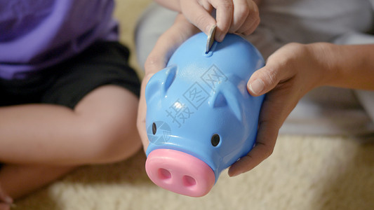 小男孩学龄前儿童幼儿园 将硬币放入蓝色面对的小猪槽投资妈妈银行母亲父母钱盒成年人预算童年教育图片