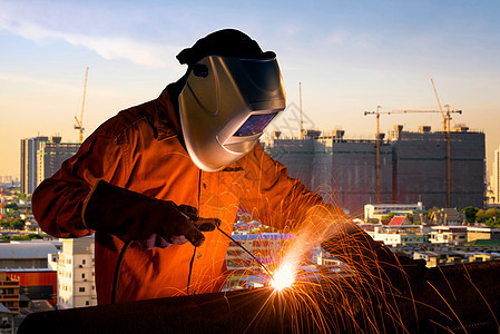工业工人为基础设施建设项目焊接钢铁结构 建筑工地在背景中具有高涨的建筑群 (单位 千美元)图片