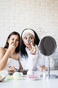 两个美丽的女人 戴上面罩 玩得开心身体女士治疗奶油乐趣皮肤毛巾护理朋友们沙龙图片