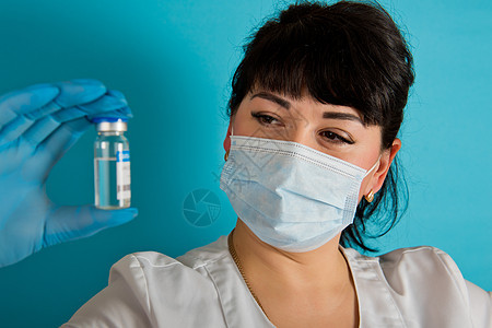 年轻护士戴着医疗面具 将Covid-19 Corona病毒疫苗的瓶子放在蓝色背景上图片