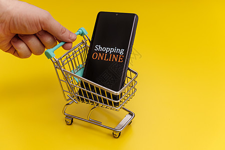 黄色背景的智能手机购物车 在线购物概念 笑声机动性零售男人命令销售网络贸易顾客技术互联网图片