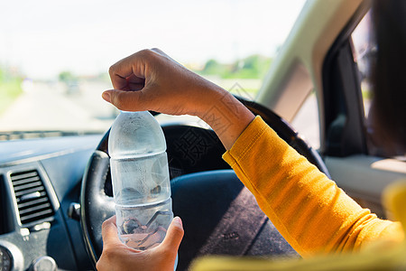 妇女驾驶汽车时用水瓶饮酒 女塑料座位成人瓶子车轮男性女士旅行女孩运输图片