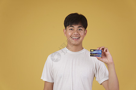 黄色背景中手持信用卡购物支付的快乐亚洲青年肖像图片