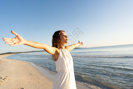 黎明时分 穿着波西米亚风连衣裙的年轻女子在海边张开双臂 望向地平线 拥抱自然概念 千禧一代嬉皮士女孩在日落时对海洋和海水的热爱态图片