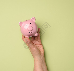 绿色背景 手持粉红色陶瓷罐头动物订金商业帐户制品玩具银行储蓄盒子经济图片