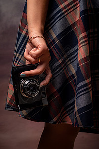 女孩的手拿着相机靠近裙子的下摆 竖框 灰色背景的工作室摄影背景图片