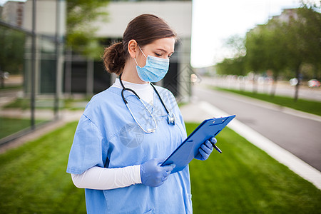 持有蓝色剪贴板 站在医院诊所街头入口外的联合王国全国保健服务女医生图片