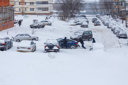 两人将卡住的现代太阳能汽车推入山坡深雪中停泊在停车场之间的一个雪院车辆帮助雪堆运输邻居季节暴风雪气候天气男人图片