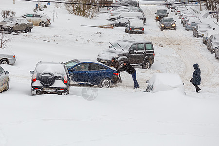 两人将卡住的现代太阳能汽车推入山坡深雪中停泊在停车场之间的一个雪院社论院子天气运输男人车辆雪堆季节社区力量图片