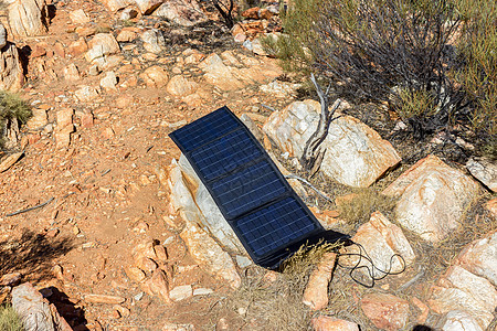 露营地岩石上的太阳能电池板为手机和相机充电 替代电源 — 可持续资源的概念图片