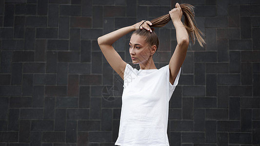 女人在早上锻炼黑墙背景前 将头发绑在马尾辫上赛跑者领带有氧运动闲暇城市运动装跑步训练女性成人背景图片