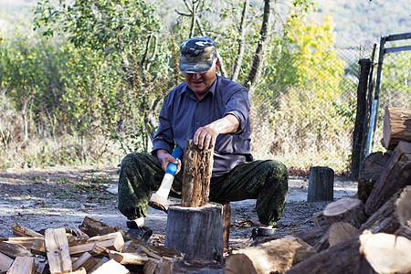 老人砍木头坐着 从前门看 白天外门闲暇木工人爱好斧头工作男性工具森林力量老年图片