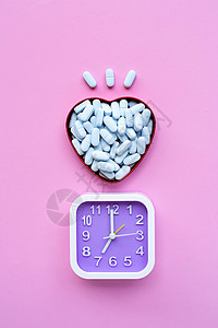 在粉红色背景的心形盒子里 装有医疗蓝药片的时钟图片